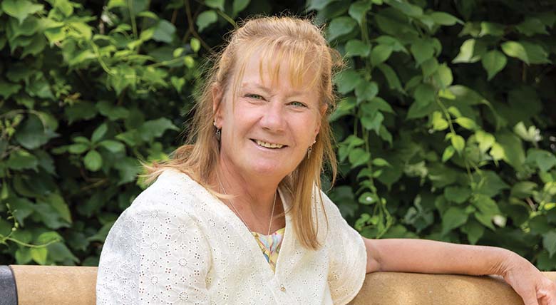 Michele Allison smiling and sitting in front of foliage after genetic testing.