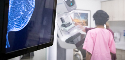 Foreground: computer image of a mammogram; out-of-focus background shot of nurse assisting a female patient during her mammogram